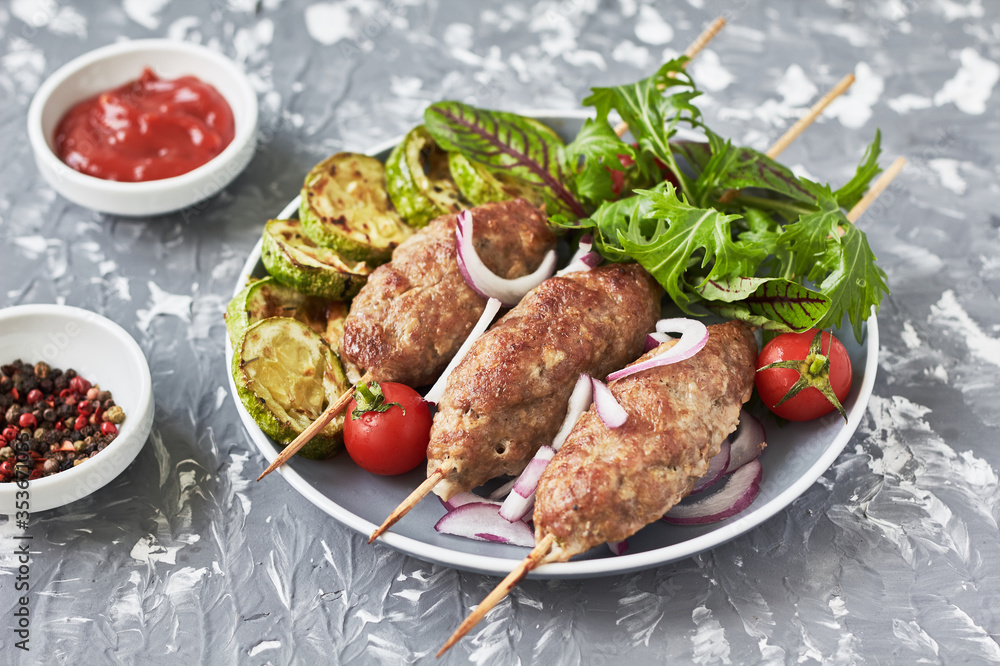 Grilled Lula kebab lamb with onions, salad, tomato and zucchini on plate. Asian traditional meat dish Grilled Lula kebab lamb with onions, salad, tomato and zucchini on plate. Asian traditional meat dish