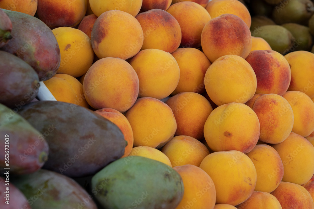 A counter with a nested pile of ripe peaches and mangoes. Selective focus.