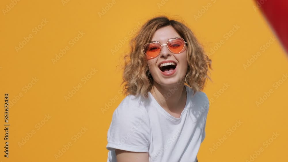 Portrait of happy woman red heart balloon holds in her hands moving from side to side in front of herself at camera, throws up ball and beats away with hand on yellow background in summer. Emotions Portrait of happy woman red heart balloon holds in her hands moving from side to side in front of herself at camera, throws up ball and beats away with hand on yellow background in summer. Emotions