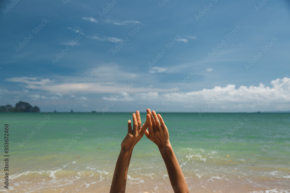 The girl's hands on the background turquoise sea and blue sky on the beach in the Golden sun The girl's hands on the background turquoise sea and blue sky on the beach in the Golden sun