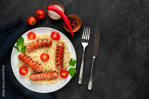 italian pasta with classic grilled sausages on a white plate with tomatoes with spices and herbs on a stone background with copy space for your text