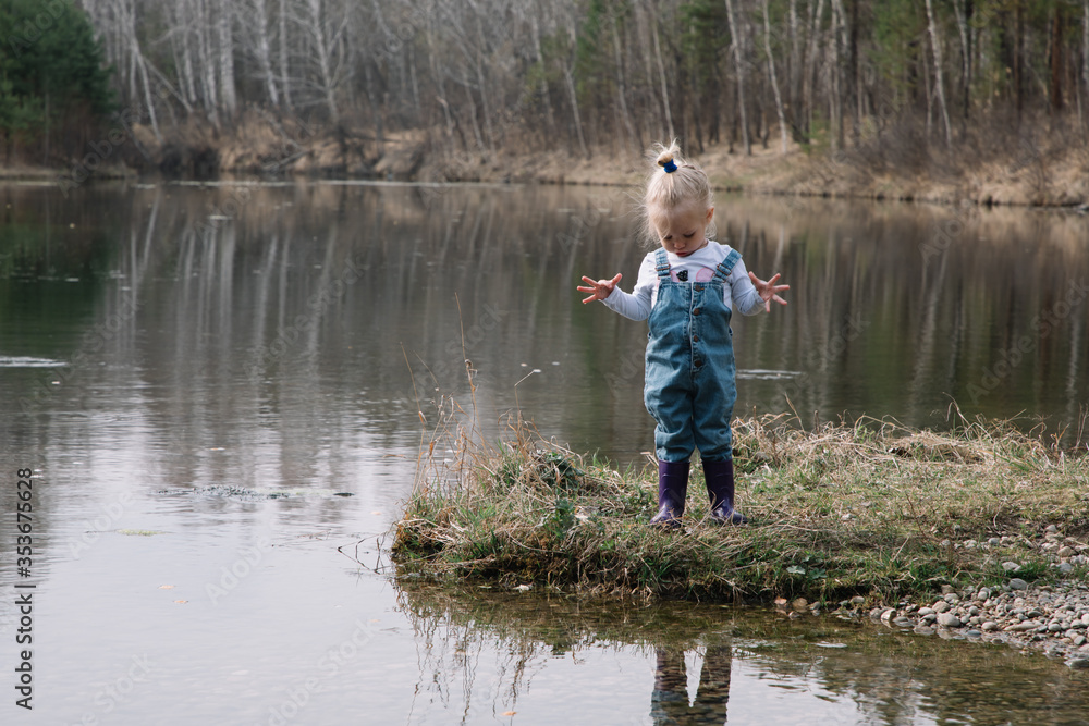 Little girl in rubber boots catches and feeds fish on the river in a jar Little girl in rubber boots catches and feeds fish on the river in a jar