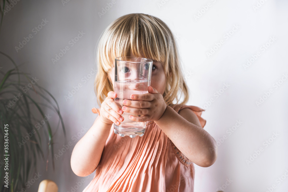 Little cute girl is sitting on a chair at home with a glass of water. The concept of a healthy lifestyle and children's health. Little cute girl is sitting on a chair at home with a glass of water. The concept of a healthy lifestyle and children's health.