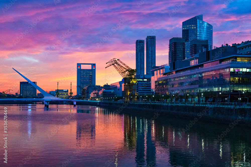 Naklejka premium Puerto Madero Bridge and city by the river, during sunrise, with colorful clouds. 
