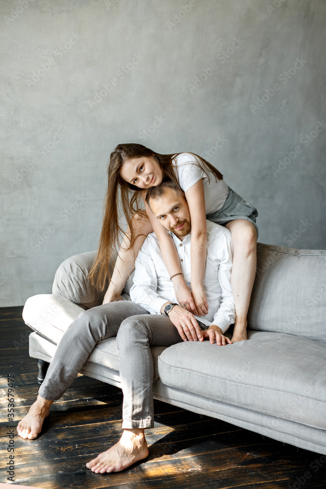Naklejka premium A young family is sitting at home on the couch and cuddling. Happy couple.On a gray background. Close-up portrait