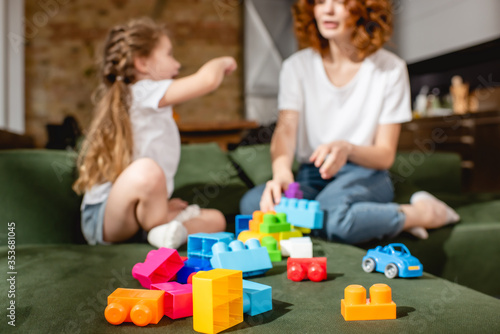 selective focus of redhead mother and cute daughter playing building blocks in living room