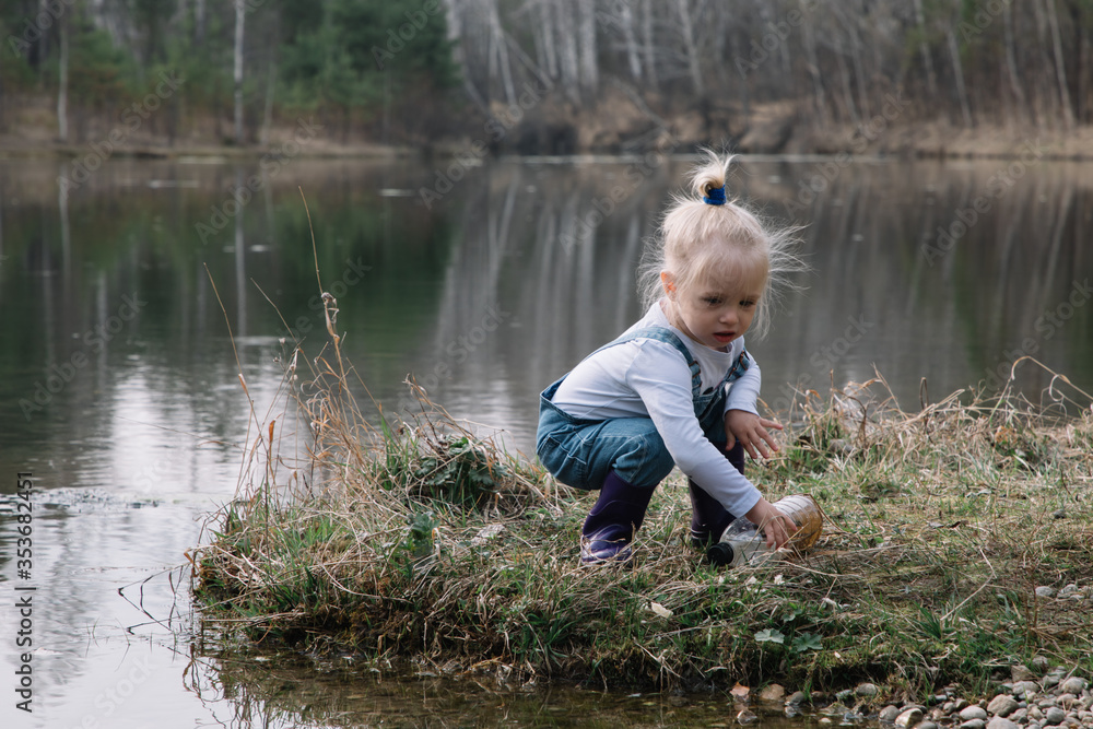 Little girl in rubber boots catches and feeds fish on the river in a jar Little girl in rubber boots catches and feeds fish on the river in a jar
