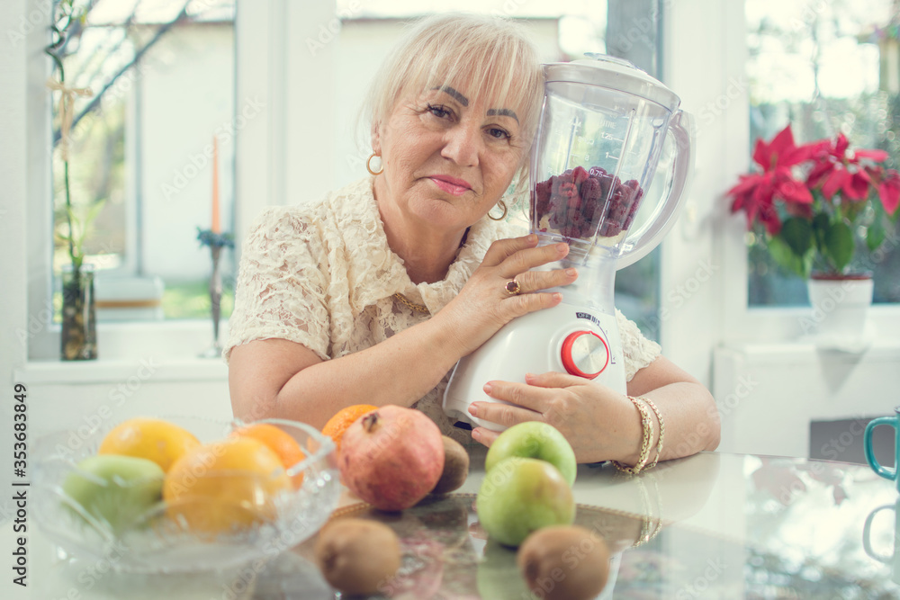 Senior woman holding blender in the kitchen. Woman preparing vegan organic smoothie at home. Senior woman holding blender in the kitchen. Woman preparing vegan organic smoothie at home.