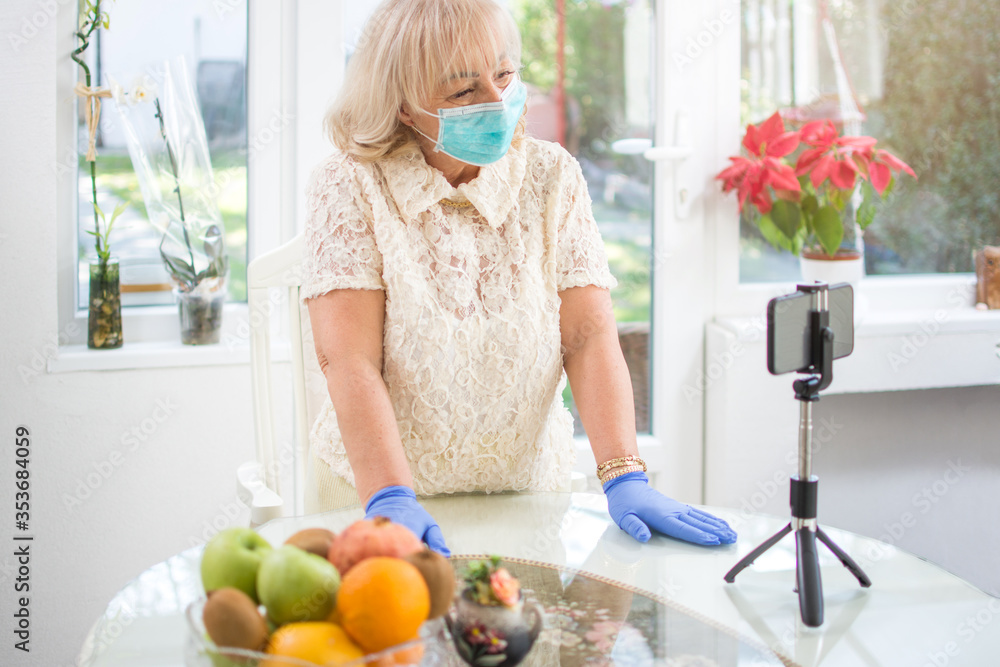 Senior woman in protective mask and gloves having a video call via smart phone at home. Senior woman in protective mask and gloves having a video call via smart phone at home.