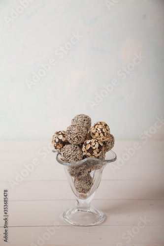 Energy balls of dried fruits with sesame seeds and granola lie in a glass vase on a white wooden table. Healthy food.