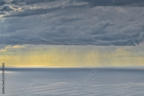 Sun shines through rain clouds over Tasman sea horizon