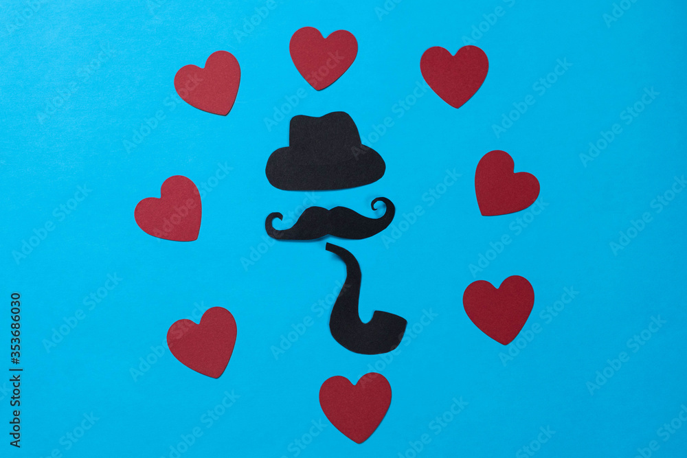 Black hat, mustache, pipe and red hearts made of paper on blue background