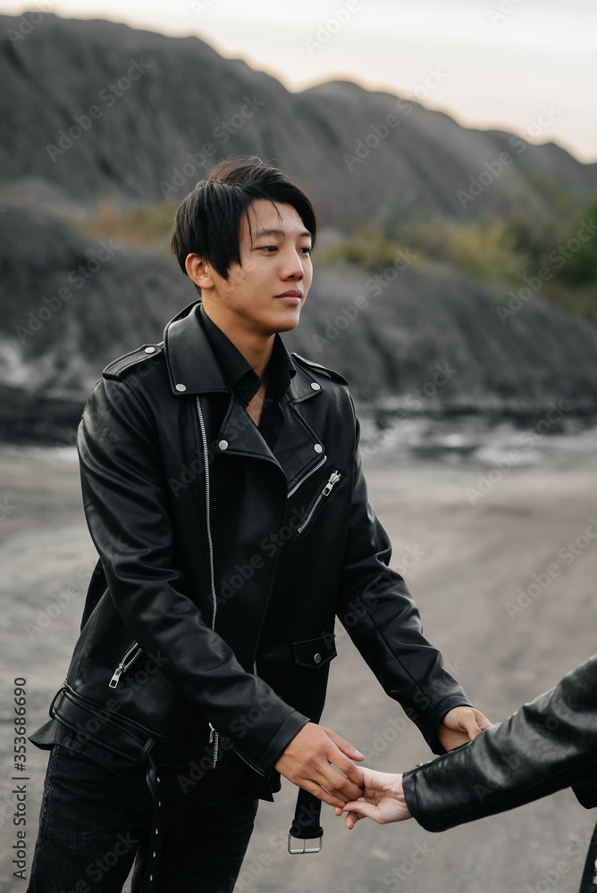 An Asian couple in love in black leather clothes walk in nature among the trees. Style, fashion, love