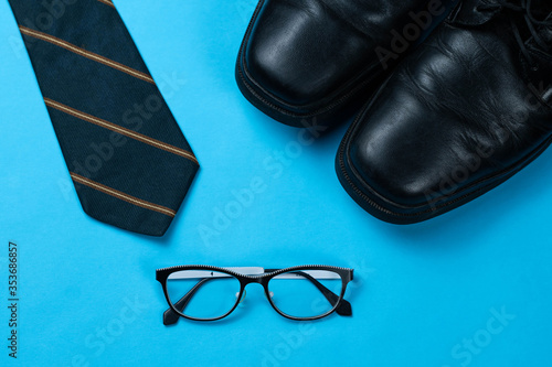 Dark tie, black formal shoes and glasses on blue background