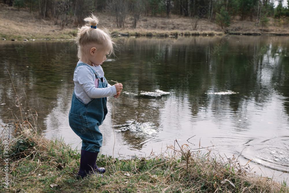 Little girl in rubber boots catches and feeds fish on the river in a jar Little girl in rubber boots catches and feeds fish on the river in a jar