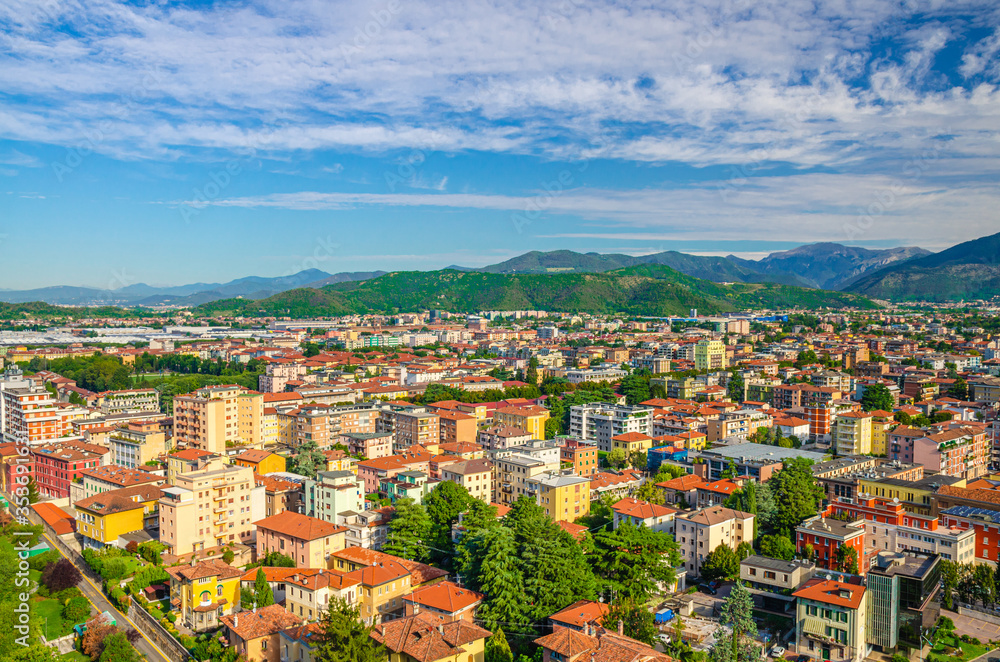 Aerial panoramic view of residential quarter with buildings of Brescia city and Alps mountain range, blue cloudy sky background, Lombardy, Northern Italy