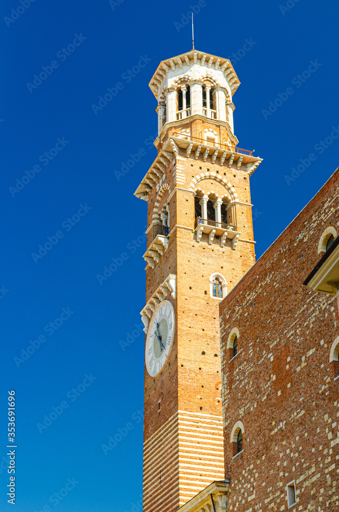 Torre dei Lamberti clock tower of Palazzo della Ragione palace building in Piazza Delle Erbe square in Verona city historical centre, vertical view, blue sky background, Veneto Region, Italy