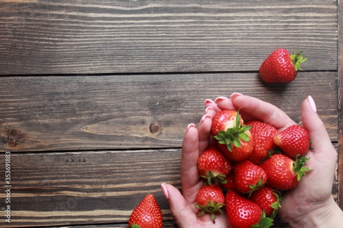 Top view of fresh strawberries in hands on a wooden table