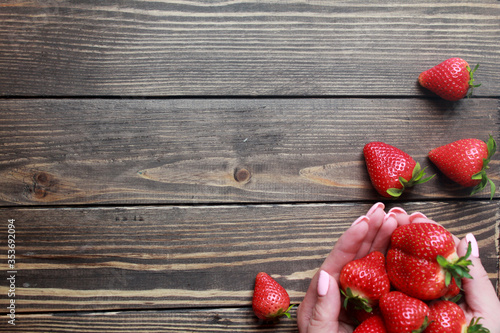 Top view of fresh strawberries in hands on a wooden table