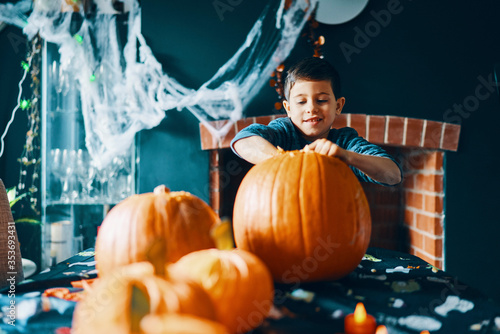 A boy with his hands in a large pumpkin on a table with pumpkins and cobwebs above. photo