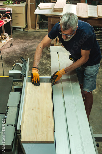 Carpenter cutting a piece of wood on the electric saw cutting machine in a wood workshop