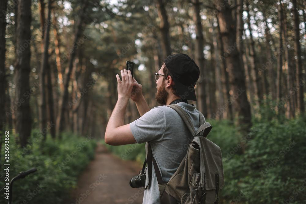 A young man tourist takes pictures on a smartphone camera in a forest. Tourism, active lifestyle A young man tourist takes pictures on a smartphone camera in a forest. Tourism, active lifestyle
