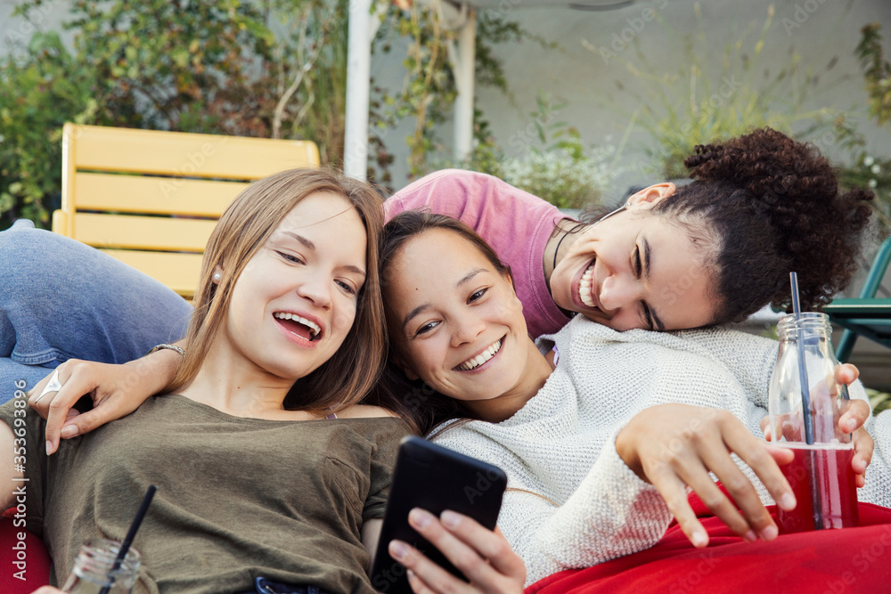 Three women lounging together, laughing and looking at a mobile phone. Three women lounging together, laughing and looking at a mobile phone.
