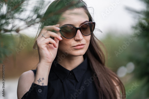 Beautiful woman with brunette hair in dark clothes and sunglasses. Fashion street photography. Fashion model is posing on nature background. sunglasses shop