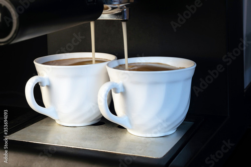 The coffee machine brews strong tasty coffee and pours it into two white mugs on a black background
