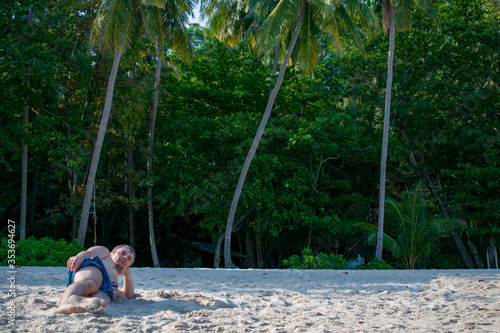 A young man in beach melts lies on the sand and sunbathes. A resting tourist poses. Beautiful landscape of exotic white sand Andamand sea beach and palm trees Southeast Asia, Thailand. photo