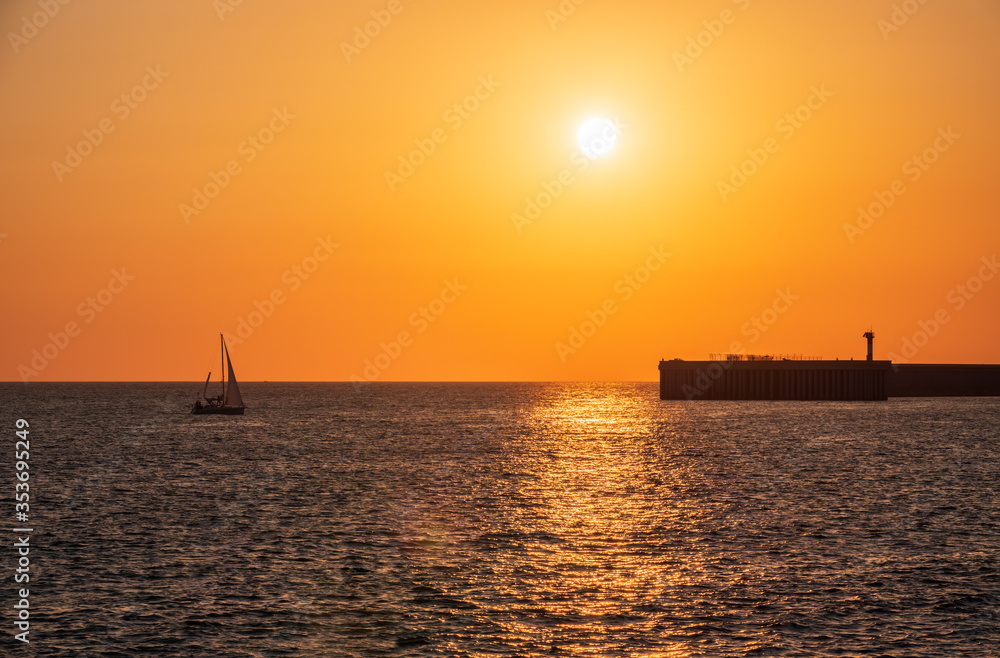 Beautiful yellow and orange sunset over the sea. The sun goes down over the sea. Silhouette of sea port at sunset