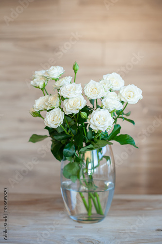 White sweet roses in soft light on a wooden background in a glass transparent vase.