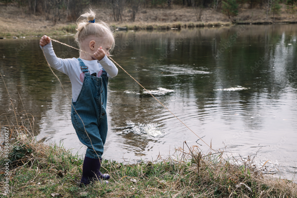 Little girl in rubber boots catches and feeds fish on the river in a jar Little girl in rubber boots catches and feeds fish on the river in a jar