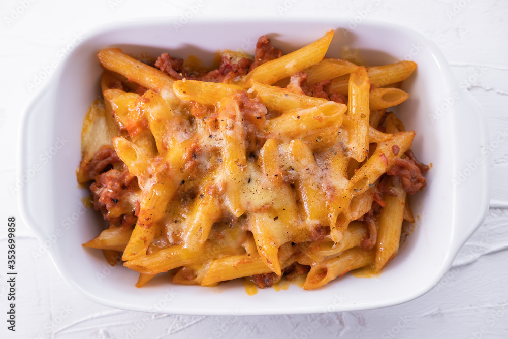 Pasta bolognesa in a baking dish with gratin cheese on white textured background. Italian cuisine. Top view. Pasta bolognesa in a baking dish with gratin cheese on white textured background. Italian cuisine. Top view.