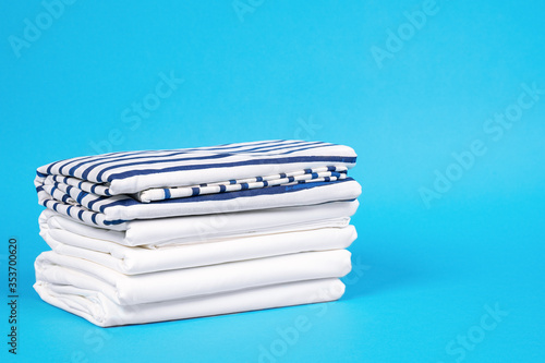 Striped and snowy white bed linen, neatly folded sheets on blue background. The concept of cleanness and proper storage organization. Copy space. photo