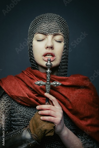 Gorgeous young woman in knight armour and steel chainmaille holding dagger on dark background. Strong and sensual woman with perfect skin and with natural makeup.