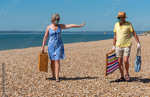 Southsea, Portsmouth, Southern England, UK. May 2020. Woman  wearing a surgical mask  social distancing from her husband during the Corvid-19 outbreak. On the beach in Southsea, UK. © petert2