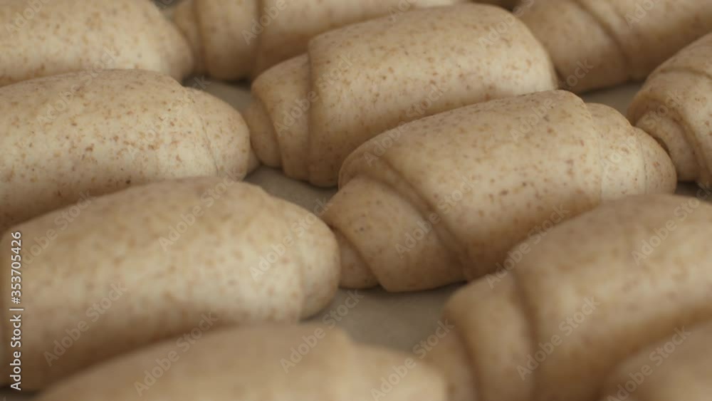 Closeup dolly shot of raw organic leavened whole wheat bread rolls or croissant in a baking sheet at the bakery. Cereal bread. Closeup dolly shot of raw organic leavened whole wheat bread rolls or croissant in a baking sheet at the bakery. Cereal bread.