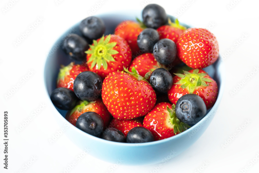strawberries and blueberries in a blue bowl on a white background close up strawberries and blueberries in a blue bowl on a white background close up