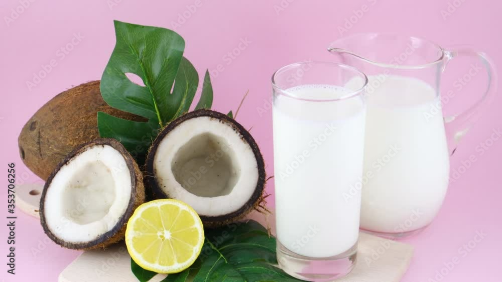 Coconut milk in drinking glass with sliced coconut and lemon on pink background Coconut milk in drinking glass with sliced coconut and lemon on pink background