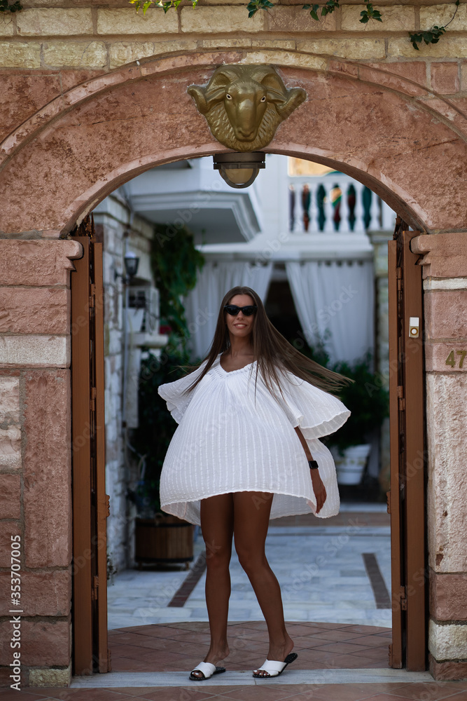 Young beautiful woman in white dress and sunglasses turns around and posing. The concept of joy, ease and freedom during the vacation. The girl is enjoying the rest. Fashion concept
