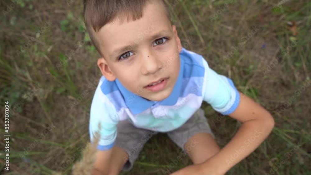 Closeup top view video portrait of beautiful cute brunette caucasian little boy smiling and laughing while looking at camera and giving thumb up gesture as sign of like and approval. Kid sits on grass Closeup top view video portrait of beautiful cute brunette caucasian little boy smiling and laughing while looking at camera and giving thumb up gesture as sign of like and approval. Kid sits on grass