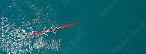 Aerial drone ultra wide photo of young women athletes rowing in canoe competition in tropical lake with emerald waters