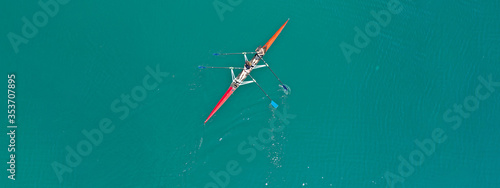 Aerial drone ultra wide photo of young women athletes rowing in canoe competition in tropical lake with emerald waters