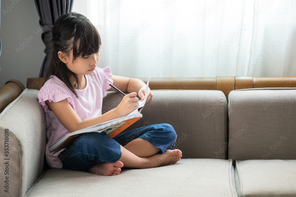 Asian little girl thinking while reading a book on the sofa in the room. Asian little girl thinking while reading a book on the sofa in the room.
