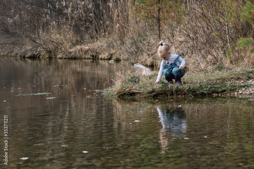 Little girl in rubber boots catches and feeds fish on the river in a jar