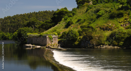 Construção em pedra antiga em forma de torre, azenha numa margem de um rio com um ramo de árvore caído, Vila do Conde, Portugal