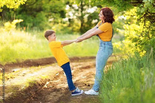 Cheerful young family: mother with a small son in casual clothes walk holding hands, play in the summer