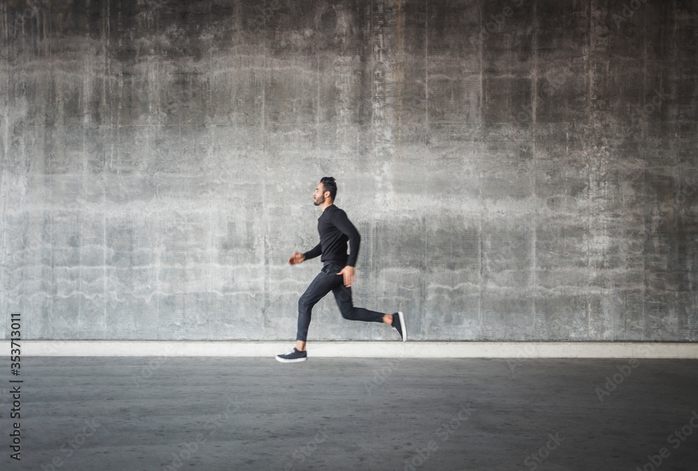 Side view of young man running by gray wall Side view of young man running by gray wall