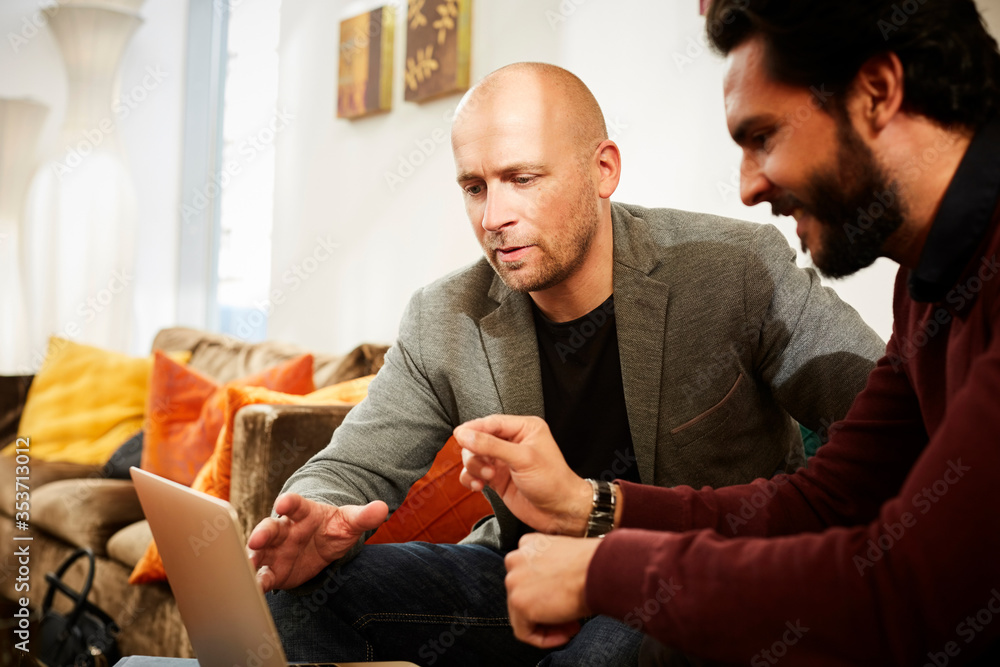 Businessmen discussing over laptop while sitting by male colleague in office Businessmen discussing over laptop while sitting by male colleague in office